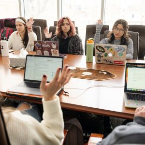 Students gather at a conference table and take a vote, raising their hands