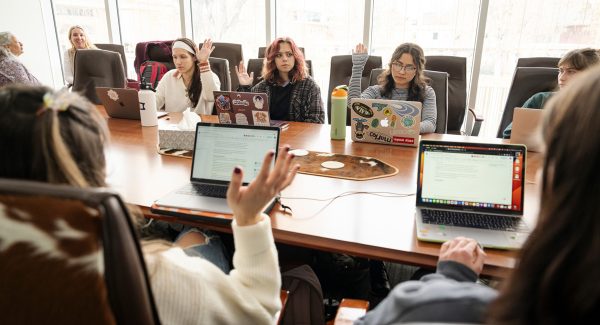 Students gather at a conference table and take a vote, raising their hands